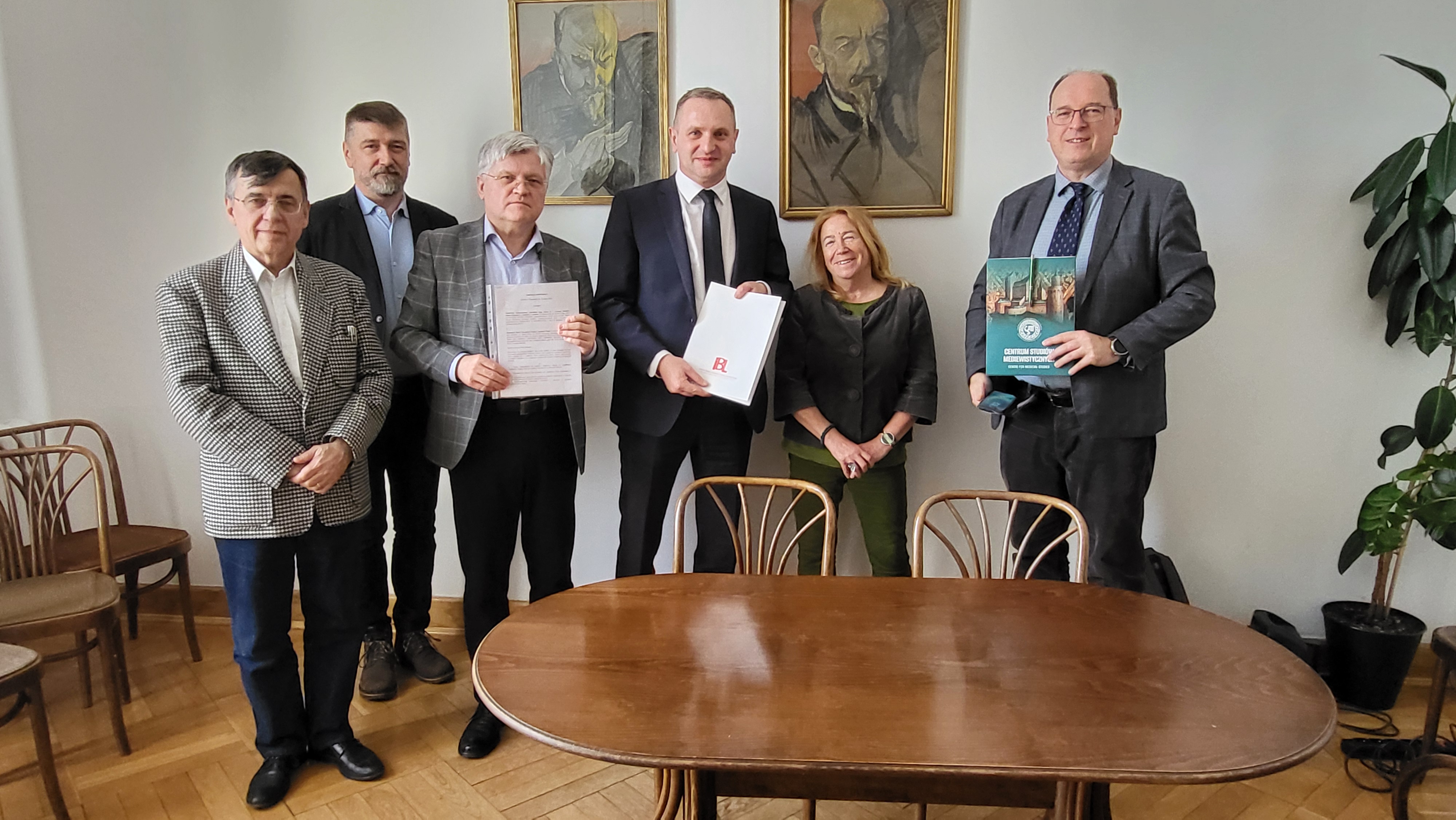 Pięciu mężczyzn i jedna kobieta pozują do zdjęcia w gabinecie dyrektora IBL PAN. Dwóch mężczyzn prezentuje podpisaną umowę o współpracy.