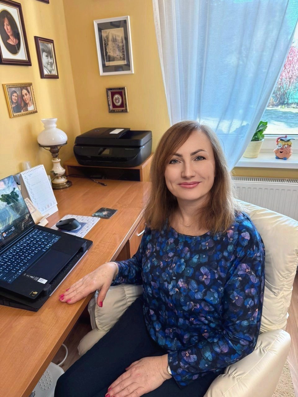 Uśmiechnięta kobieta siedząca przy biurku, oderwana od pracy na laptopie.